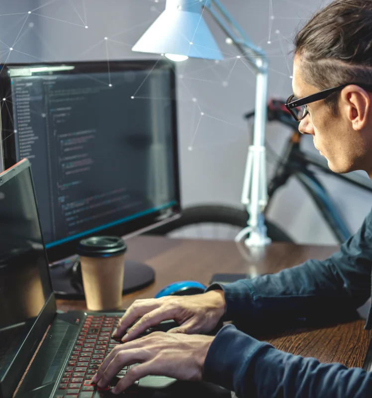 Software developer coding on a laptop and monitor setup in a modern home office with digital connectivity graphics.