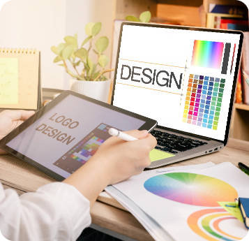 A person using a stylus on a tablet labeled “Logo Design” while working on a laptop displaying a design interface with color palettes, alongside printed color charts on a desk.