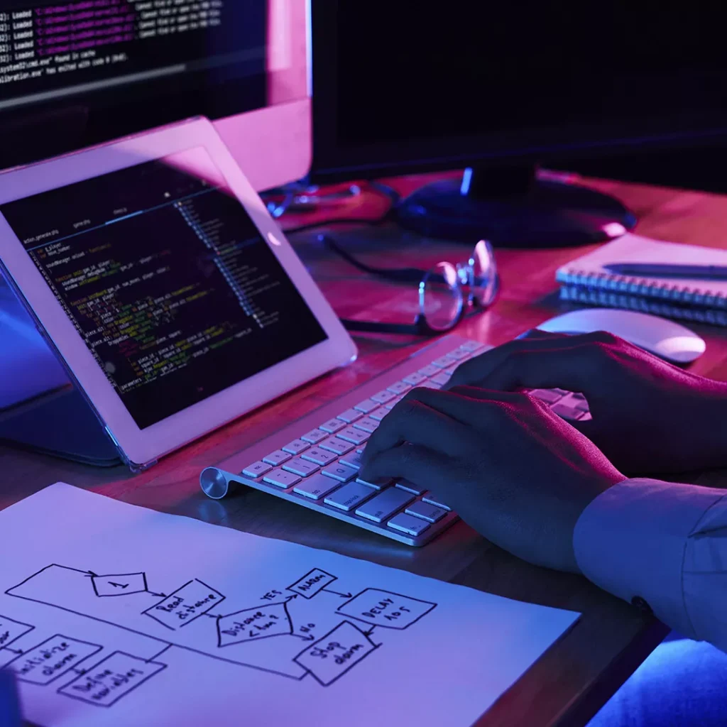 Software engineer developing code and logic flowcharts for a technical project in a modern, neon-lit workstation.